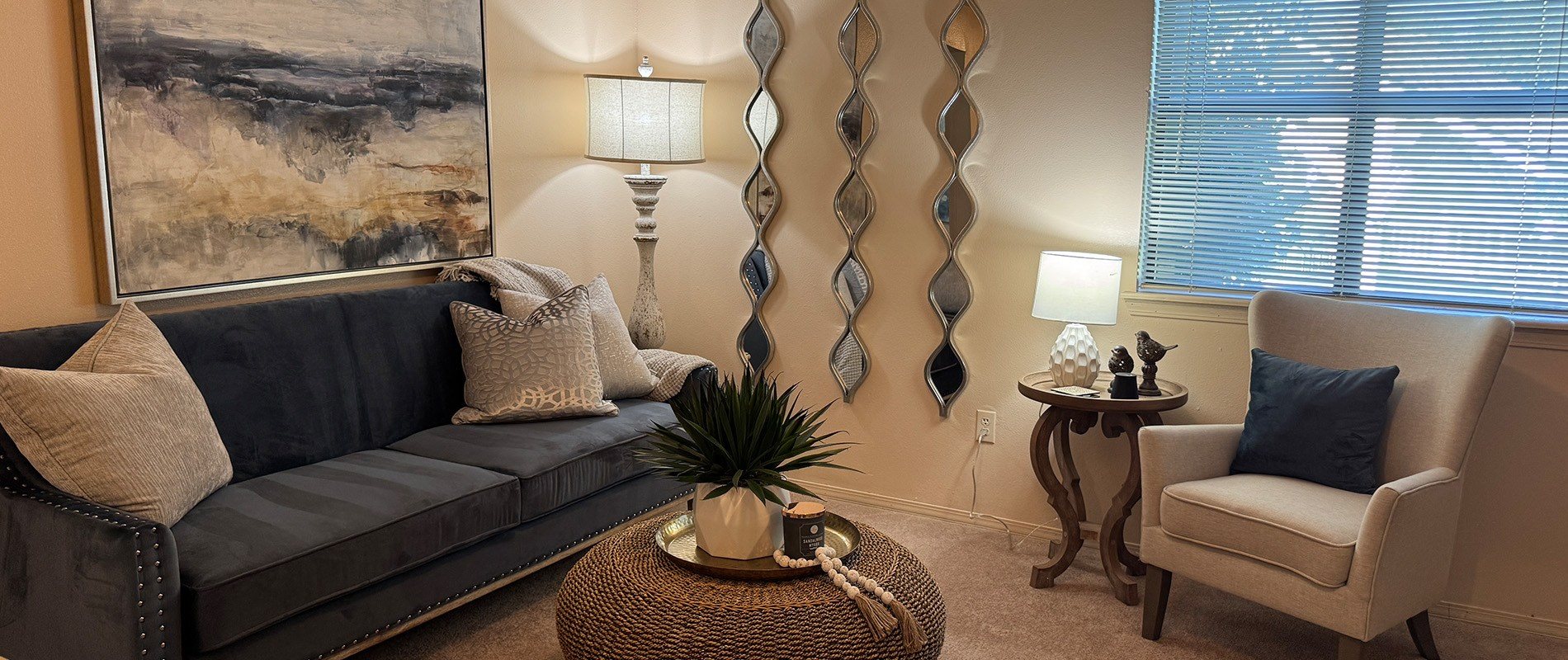 A living room with a grey couch, a small table with a plant on it, and a wall with a large painting.